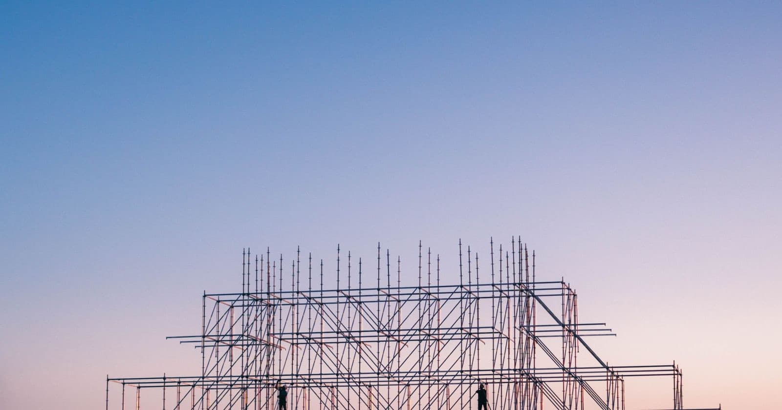 Silhouette of workers on tall scaffolding framework against a pink and blue dusk sky