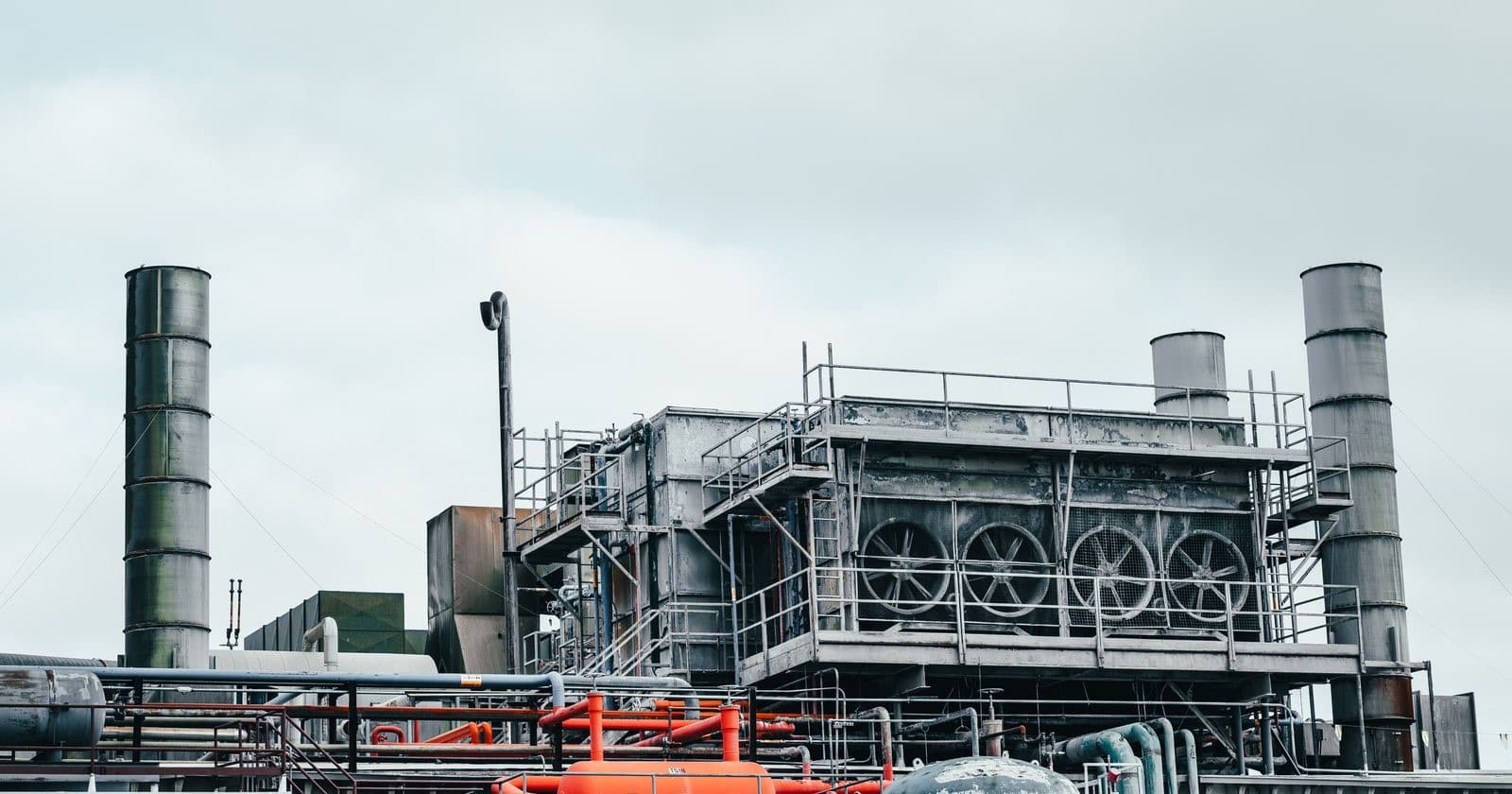 Industrial plant with tall chimney stacks, pipework and cooling units against a pale sky