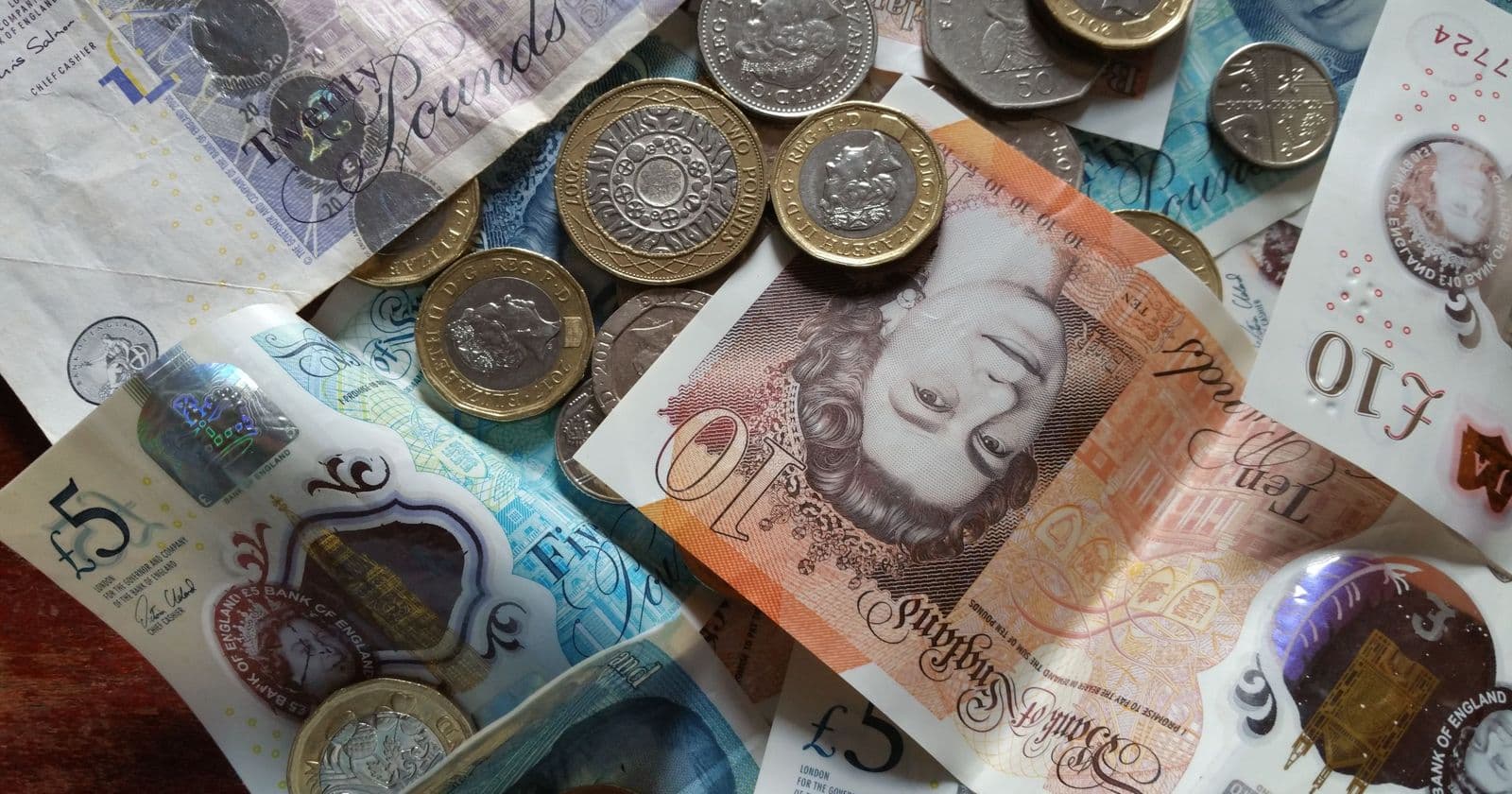 Scattered British pound coins and polymer five and ten pound banknotes on a table