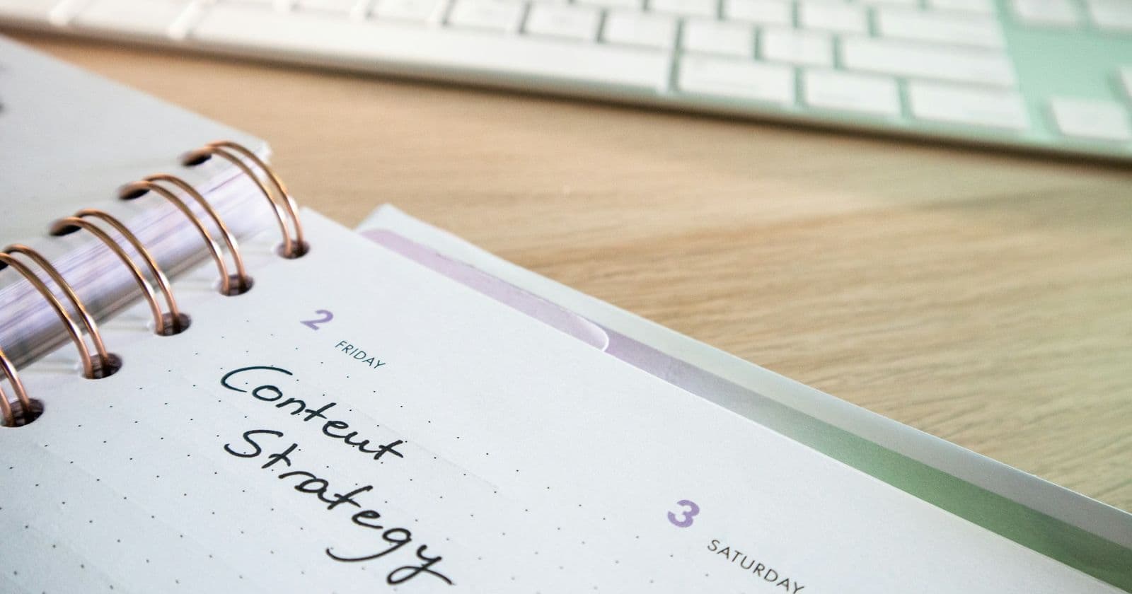 Stock photo: Spiral desk planner open at a page handwritten Content Strategy beside a computer keyboard on a wooden desk
