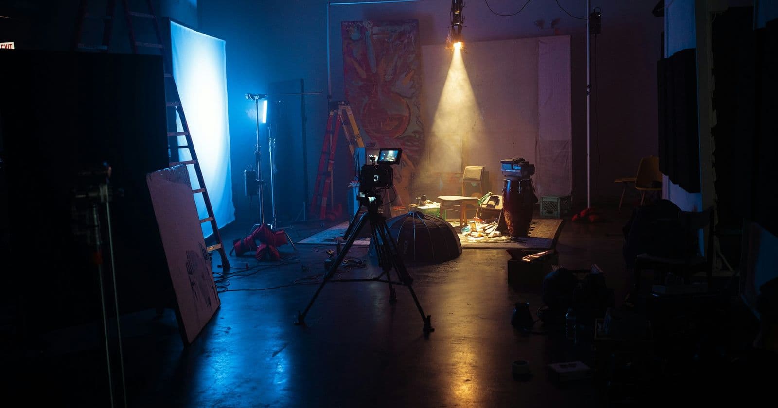 Stock photo: Dim film studio with a camera on a tripod, a monitor, and a single spotlight beam through haze