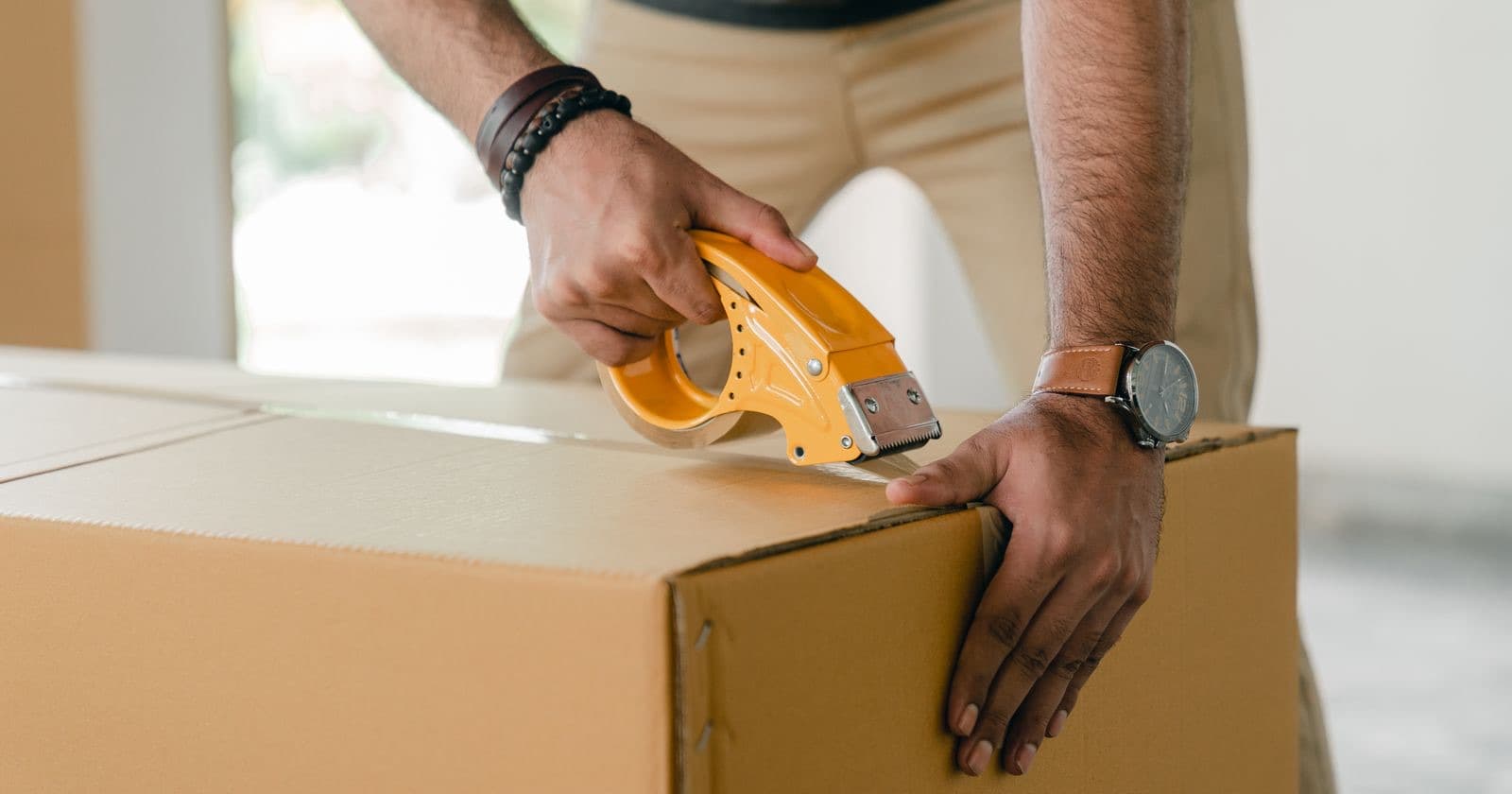 Stock photo: a man sealing a cardboard box with a tape dispenser