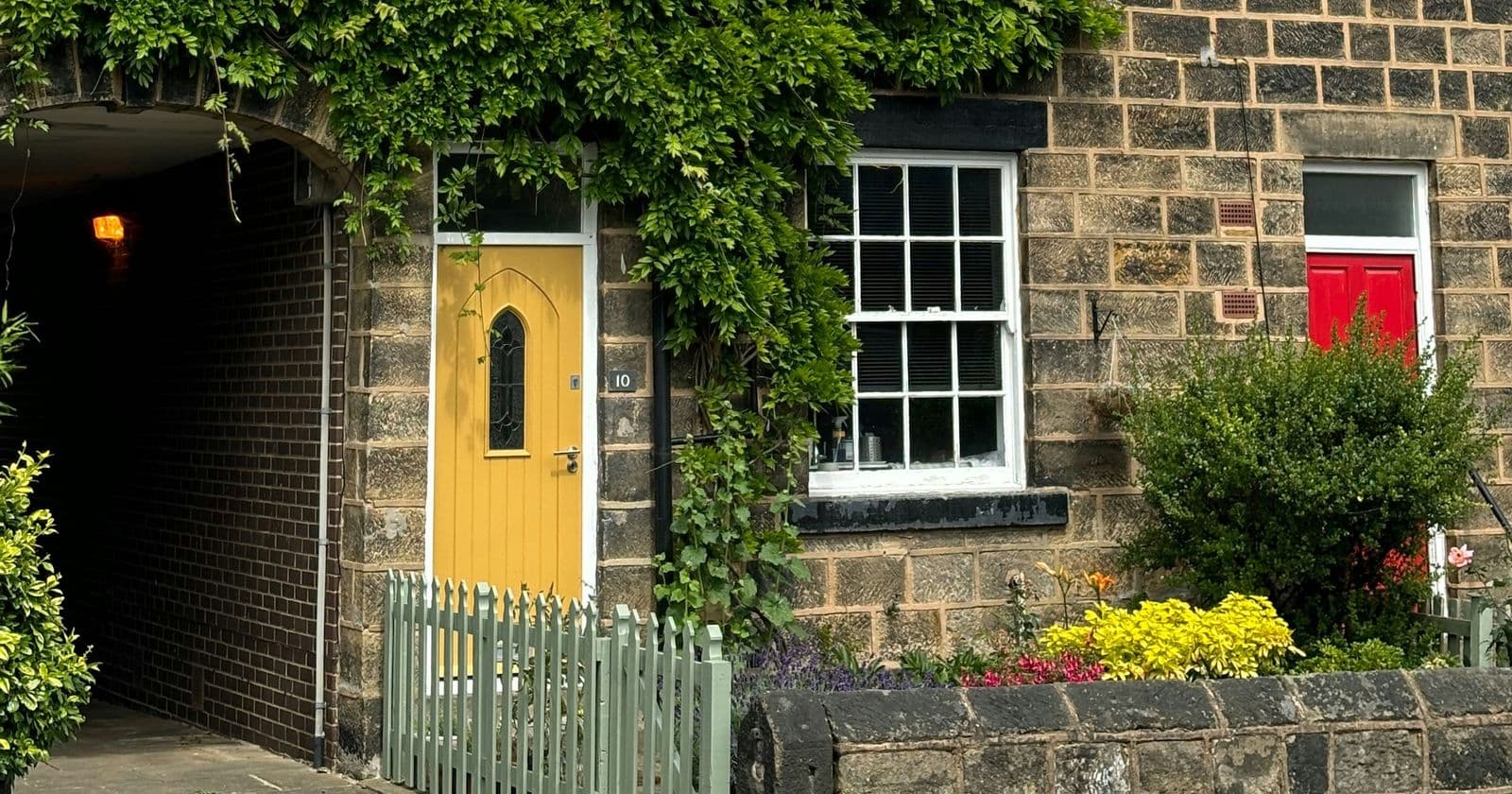 Stone-built terraced houses with white-framed windows, a yellow front door and a climbing plant beside a green picket fence