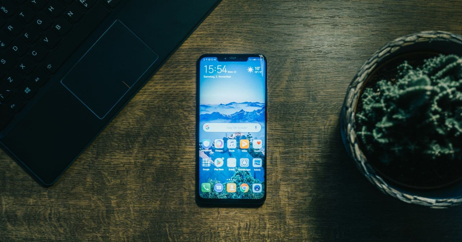 Smartphone lying on a dark wooden desk beside a laptop keyboard and a potted succulent, seen from above