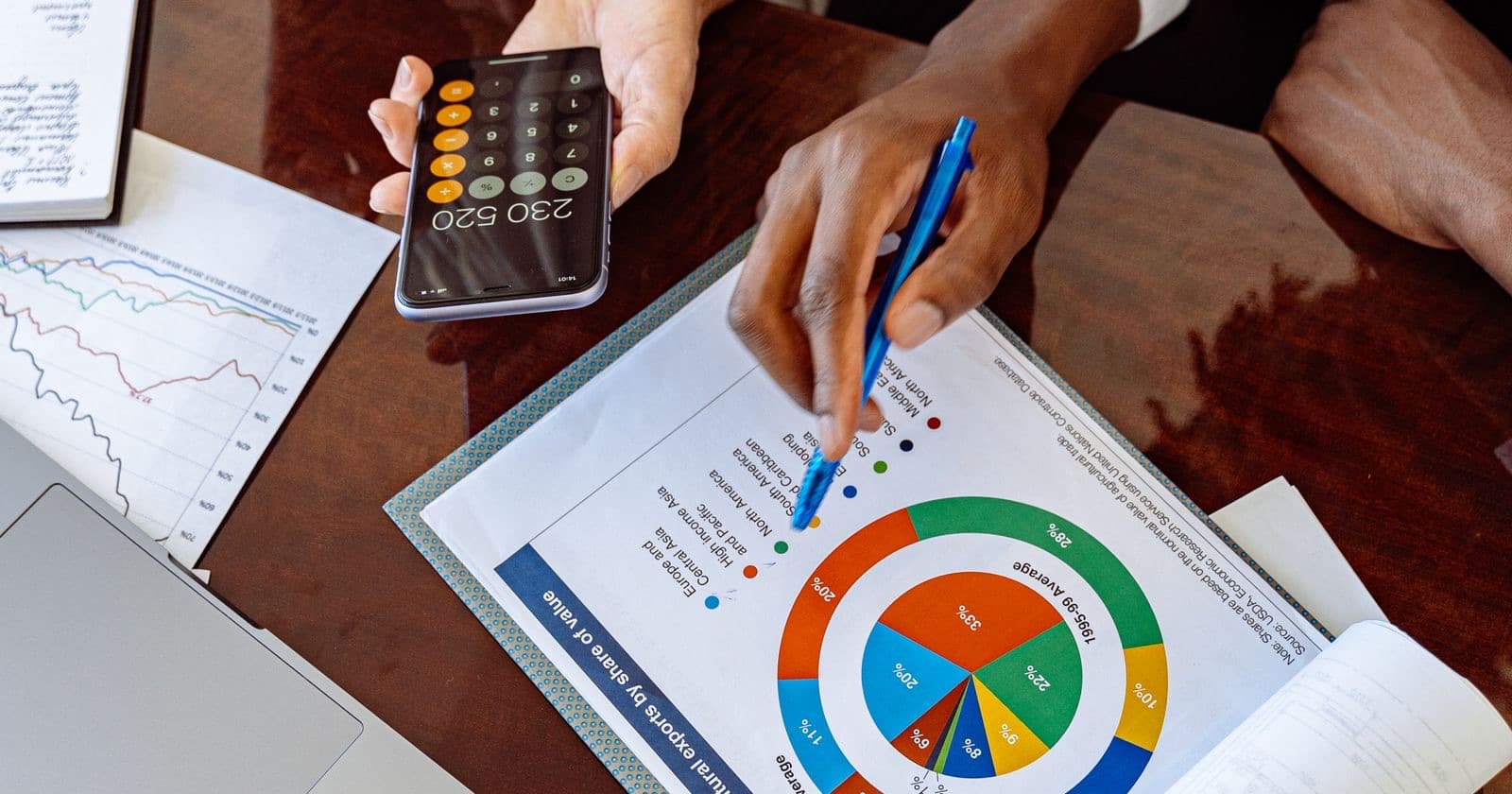 Hands with a pen, calculator and printed donut chart on a desk during a financial analysis