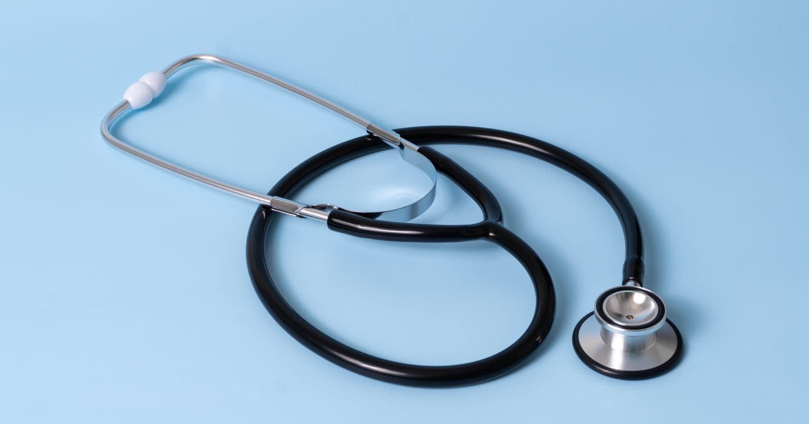 Black stethoscope laid on a plain light blue background
