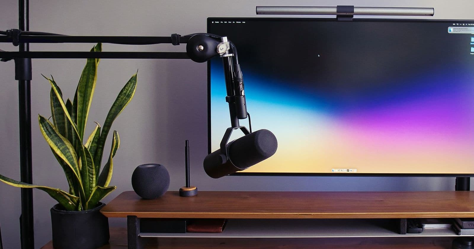 Wooden desk with boom-arm microphone, large monitor, plant and softbox light, set up for recording video content
