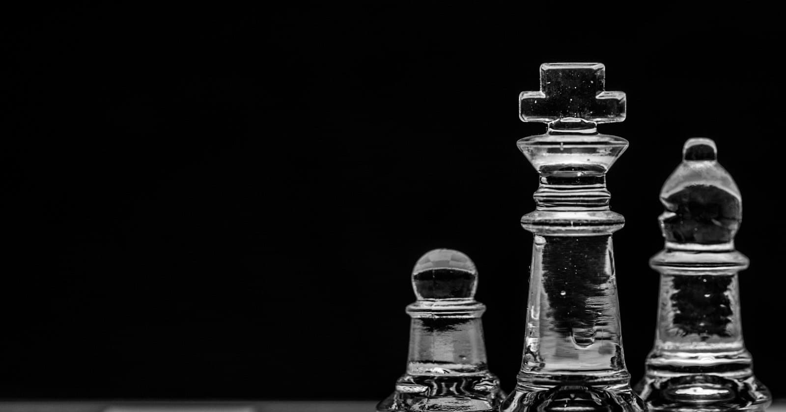 Clear glass chess king, pawn and bishop against a black background