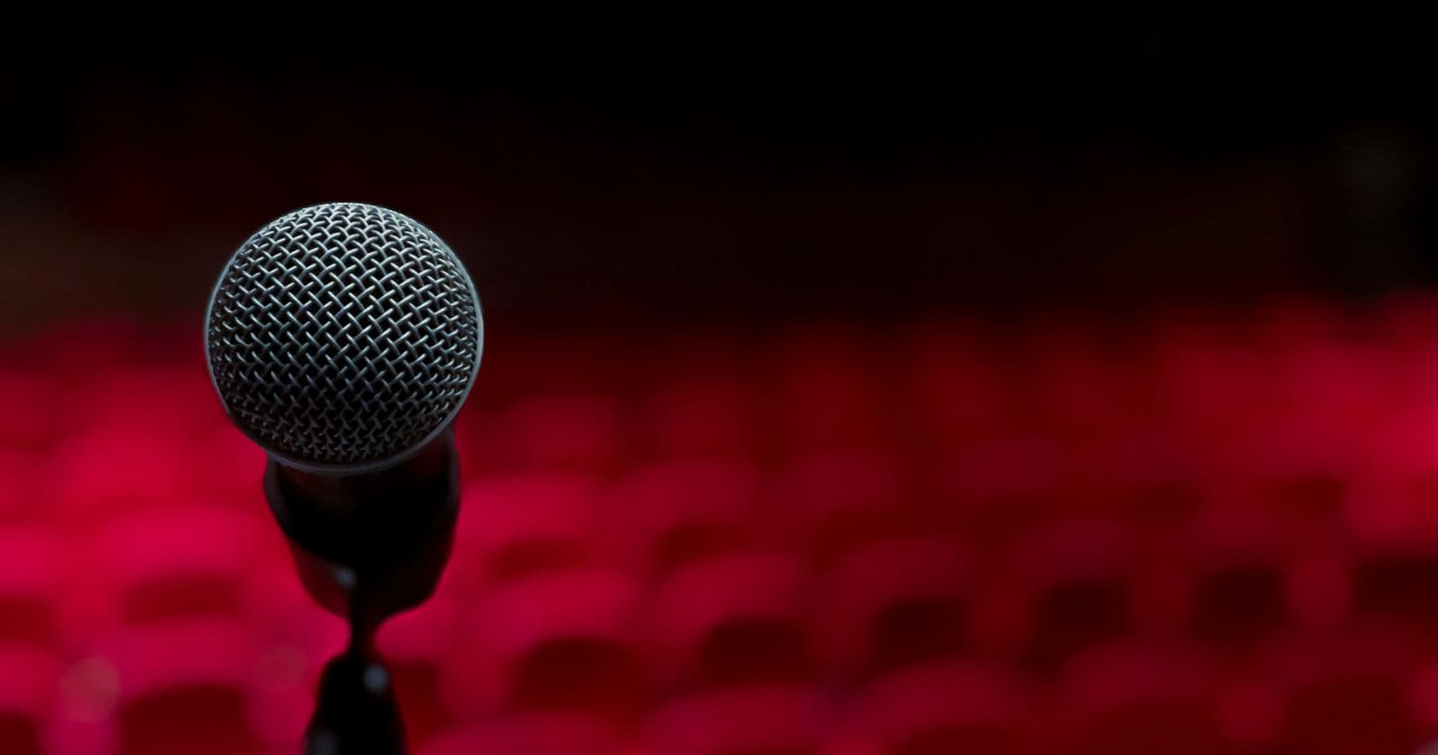Close view of a microphone on a stand with rows of empty red theatre seats blurred behind it