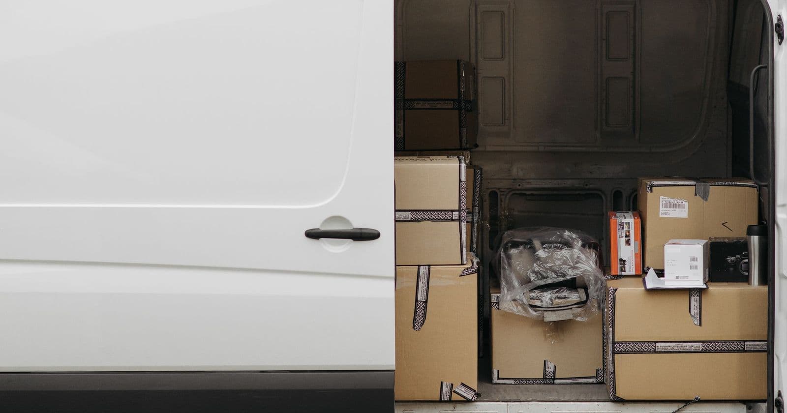 White unmarked van with its side door beside the open rear, loaded with stacked cardboard boxes
