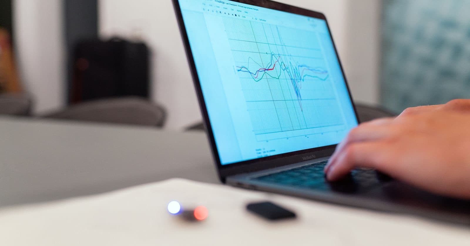 Hand typing on a laptop displaying a line graph of data on a desk