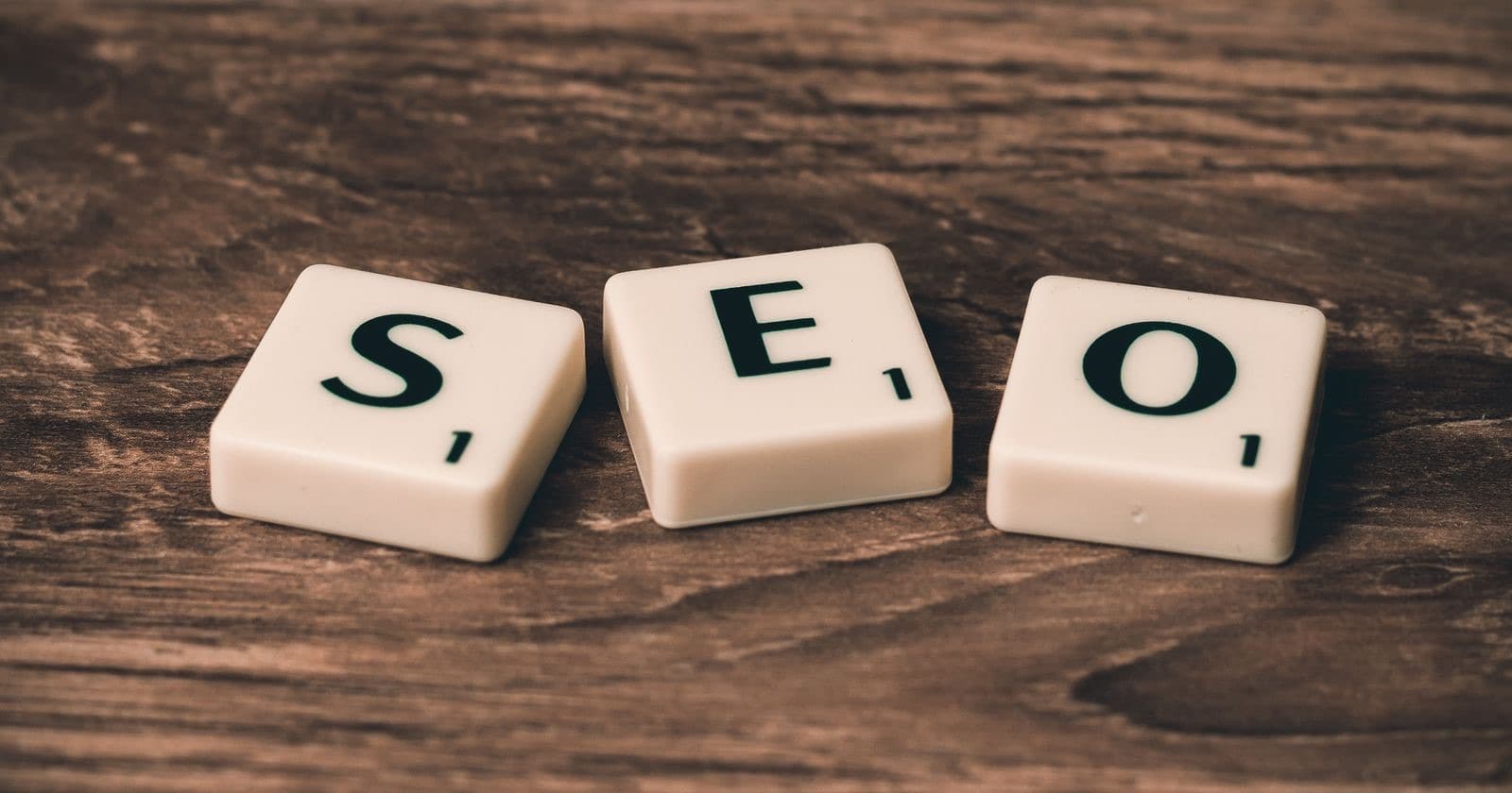 Three Scrabble-style letter tiles spelling SEO on a dark wooden table