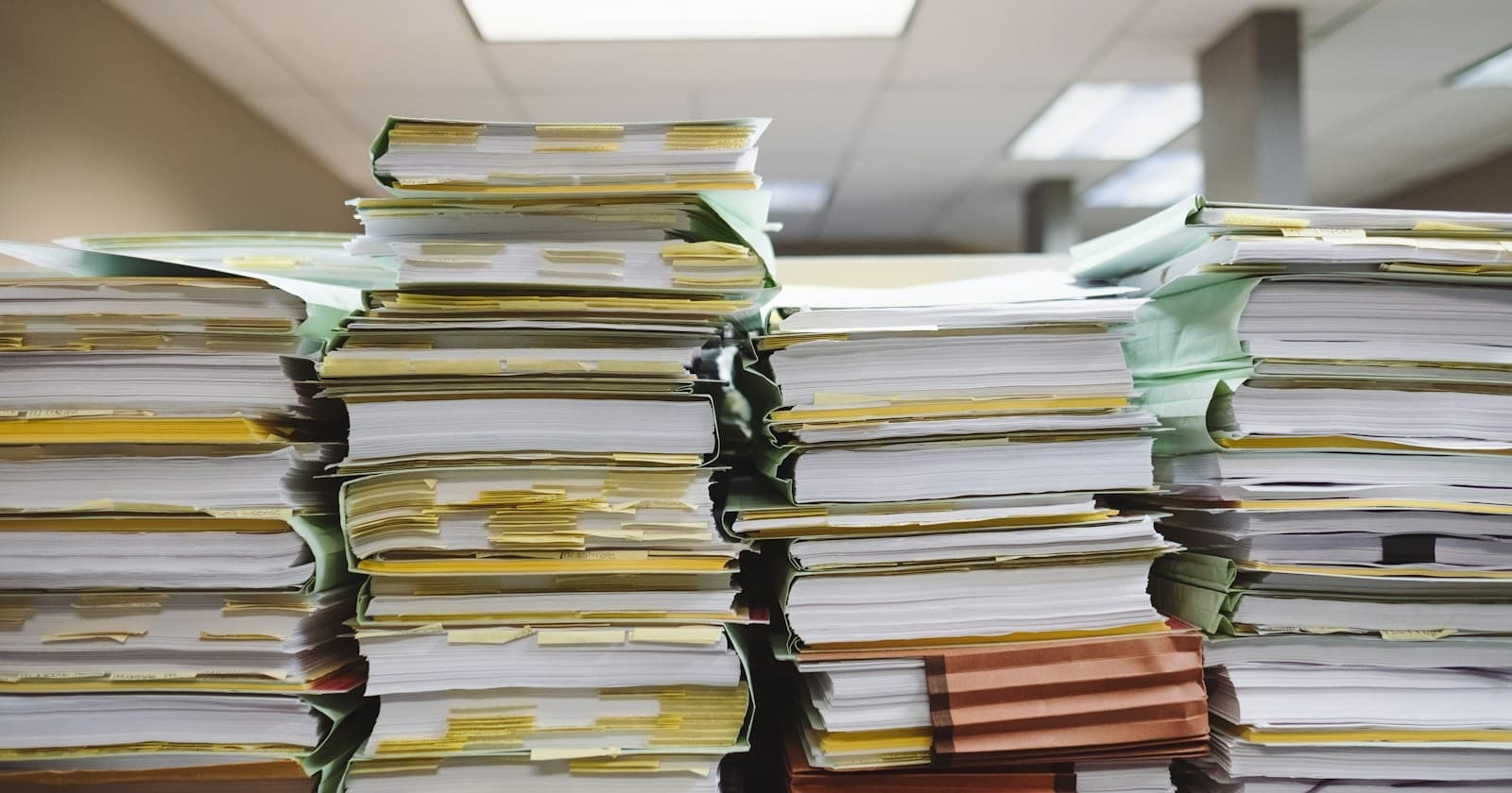 Tall stacks of paper files and folders with yellow sticky tabs in an office