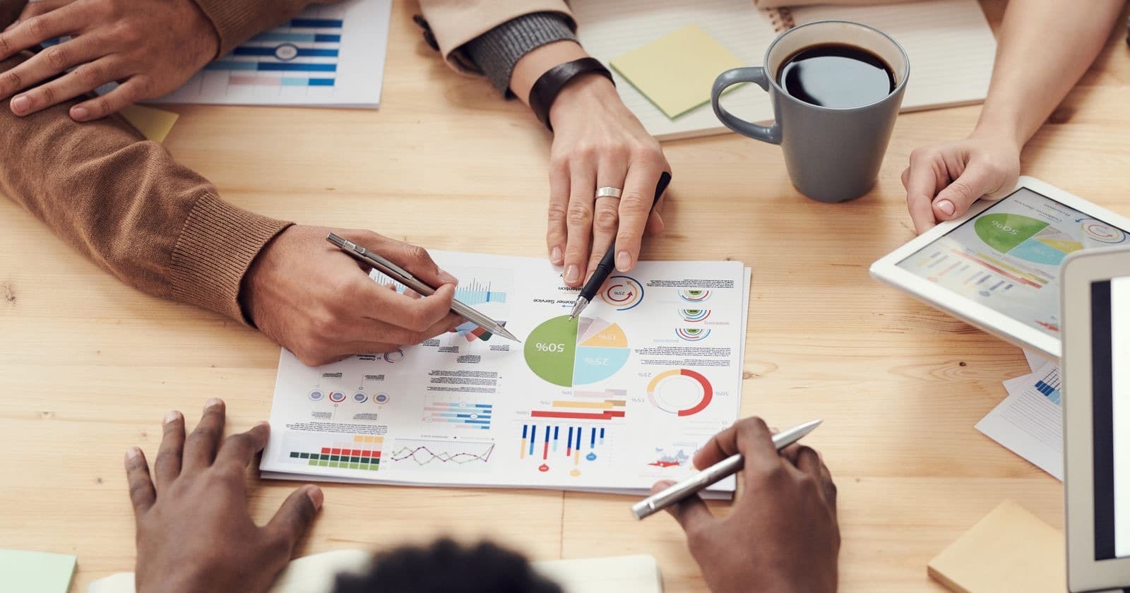 Overhead view of colleagues' hands pointing at printed pie and bar charts on a table