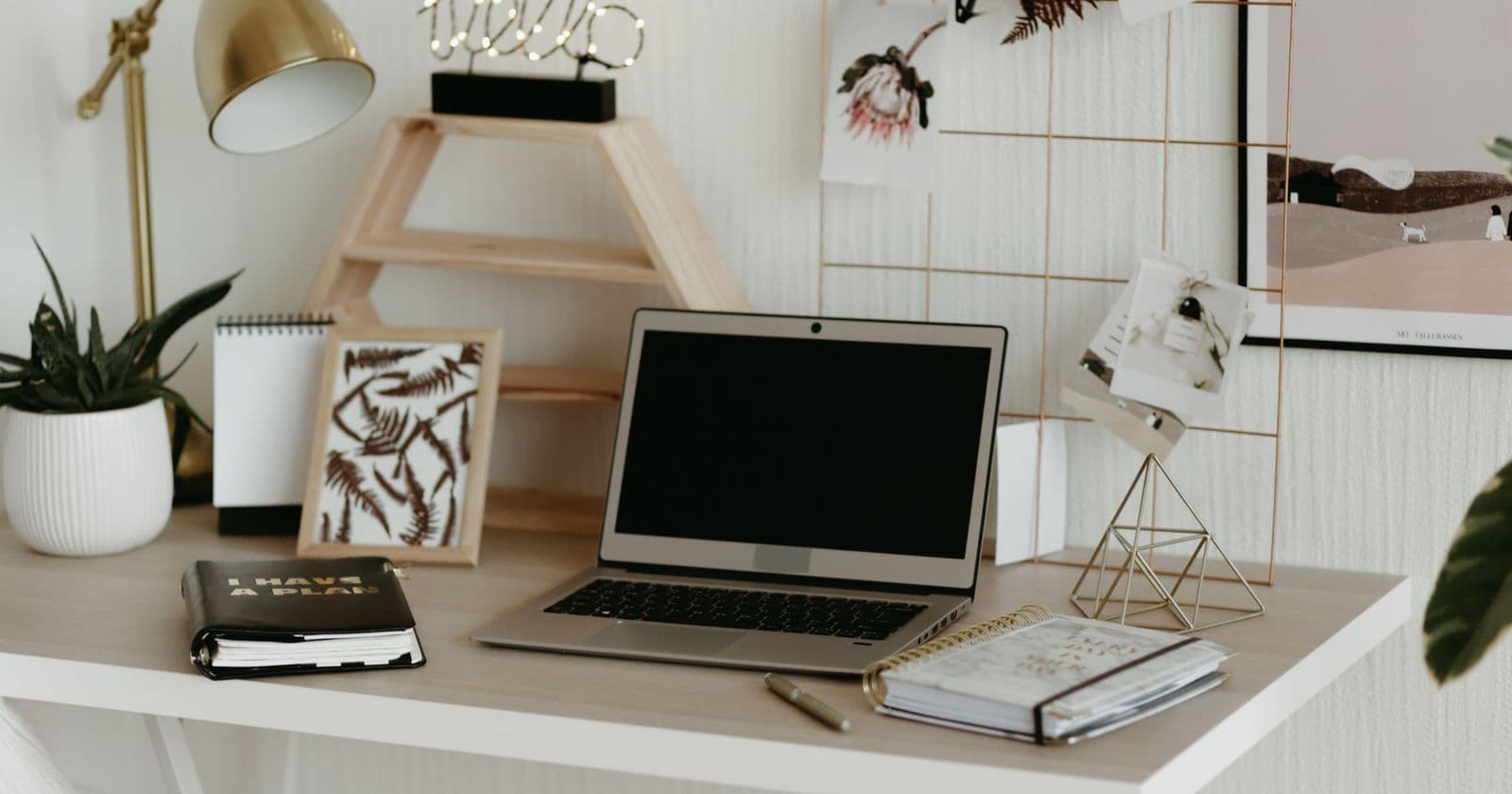 Tidy white desk with a laptop, notebooks, pen, lamp and plants in a bright home office