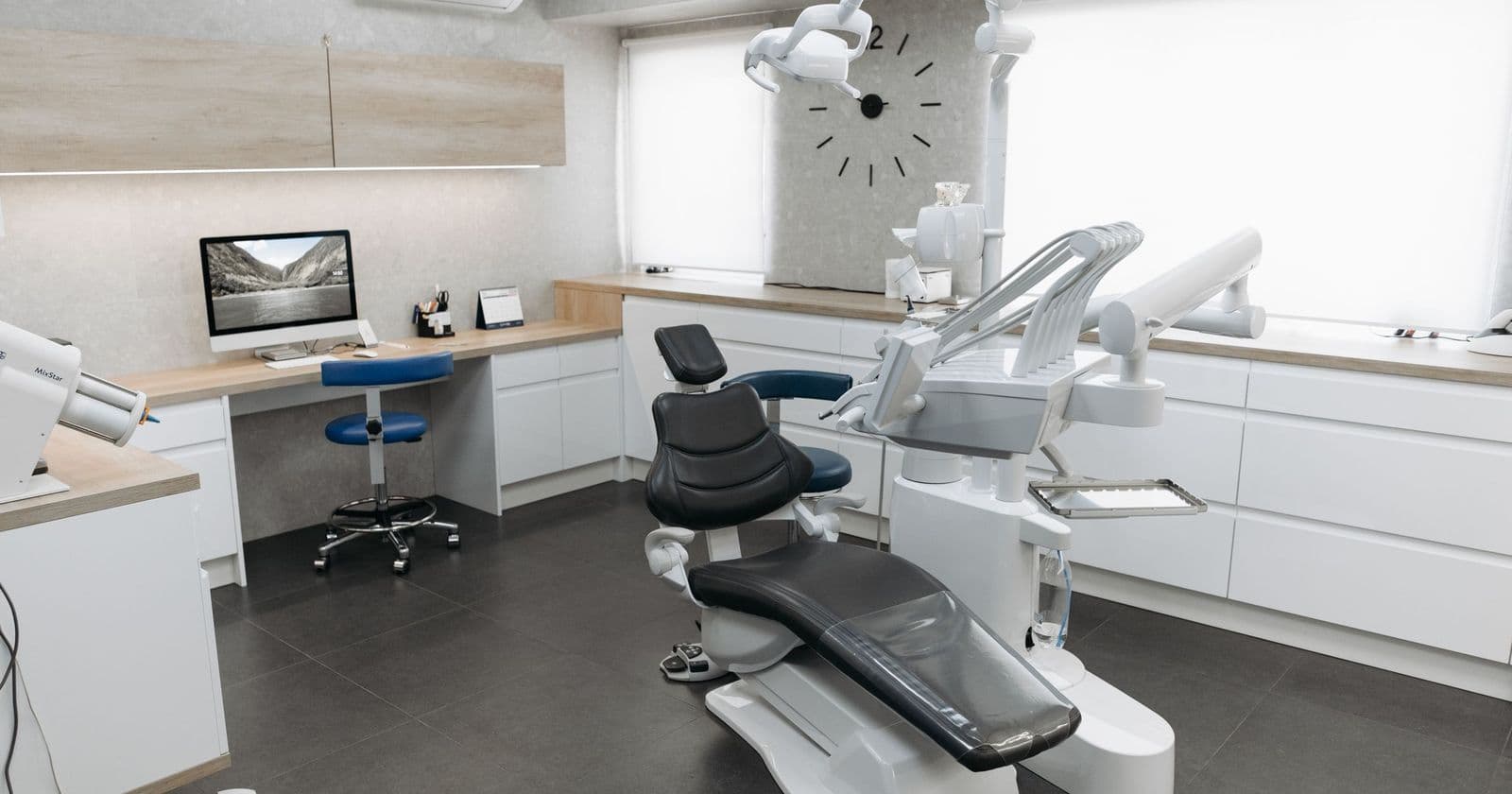 Empty modern dental surgery with a black treatment chair, white cabinets and a computer on the desk